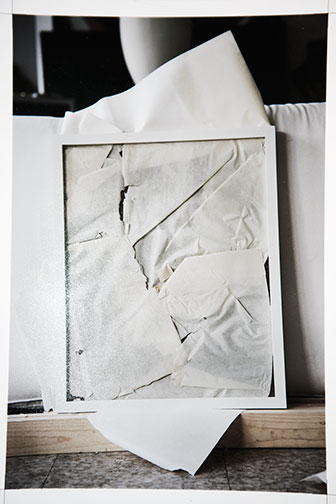 Stack of white prints and brown packing paper draped over framed works in a studio