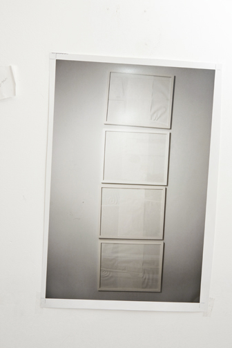 Four framed works stacked vertically on a wall, each covered with translucent white paper